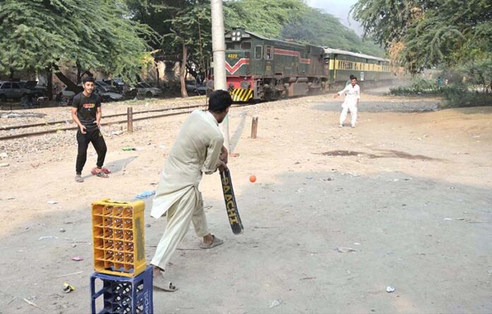 Youngsters enjoy a game of cricket near the railway track at Tewana Park, with a train approaching in the background