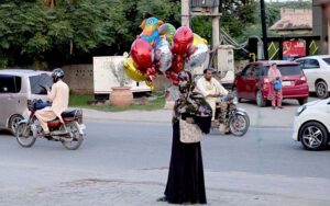 A burqa-clad woman sells colorful balloons on Club Road, trying to earn bread for her family in the streets of the city