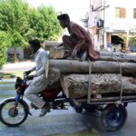 A motorcycle cart loaded with tree trunks passes through the streets of Bahawalpur