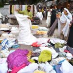 Women selecting and purchasing old clothes pieces from roadside vendor at Kohati area