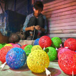 A young vendor prepares to sell beautifully decorated electric lamps at the roadside, aiming to attract customers with their vibrant designs