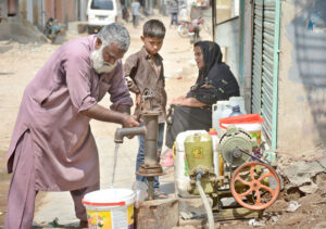 An elderly person getting water through hand pump in a street.