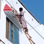 A worker painting a building along the roadside in the city