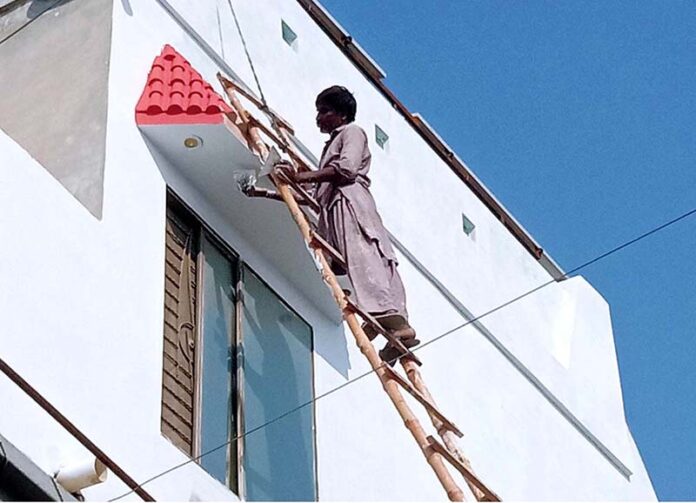 A worker painting a building along the roadside in the city