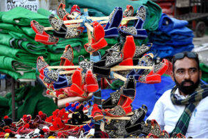 A vendor patiently waits for customers to buy handmade children's shoes at a roadside setup in the provincial capital