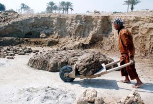 A laborer transports mud on a cart after mixing it for brick-making.