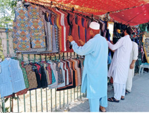 People are buying waistcoats from a stall on the side of the road.