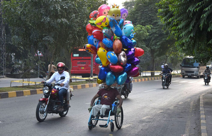 A disable person on the way for selling the colorful balloons while shuttling on the road on their wheel chair to earn for livelihood
