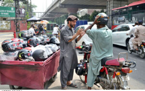 A motorcyclist tries on the right size helmet to buy from a roadside handcart in order to comply with traffic regulations.
