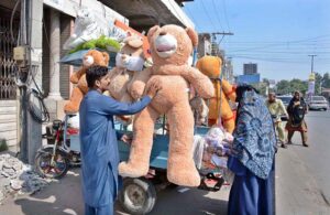 A roadside vendor sets up a colorful display of large, cuddly soft toys, hoping to catch the eye of passers-by in the city.