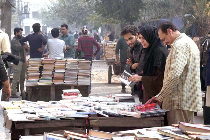 People selecting and purchasing old books from a roadside stall at Mall Road in Provincial Capital