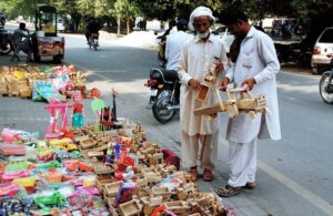A man selecting to buy handcrafted wooden tractor trolleys toy for kids from a roadside stall in the city.