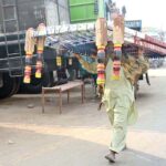 A vendor is carrying traditional bed (charpai) on his head shuttling on the road and trying to sell it