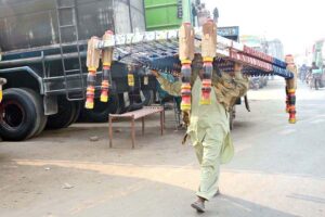A vendor is carrying traditional bed (charpai) on his head shuttling on the road and trying to sell it