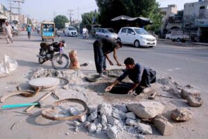 Municipal Corporation workers repair an open sewage manhole on the main road to ensure public safety.