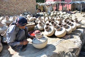In the countryside, a potter meticulously paints clay pitchers used for water storage, preserving an age-old craft in his workshop.