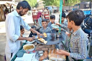 School children gathering around a street vendor, eagerly buying burgers outside a local school, adding street food culture to their day.