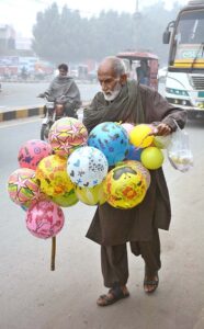 An elderly street vendor selling colorful balls while shuttling on the road.