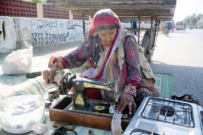 An elderly woman stitching clothes and selling kitchen items on footpath