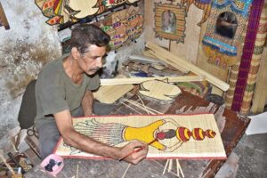 An artist busy painting on bamboo sticks and cloth at his workplace in a local market of Provincial Capital.