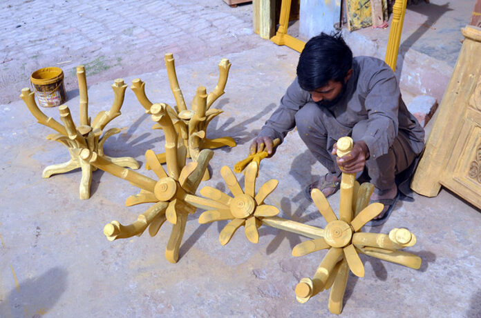 A skilled worker colours hanging stand at Shahdara Furniture Market
