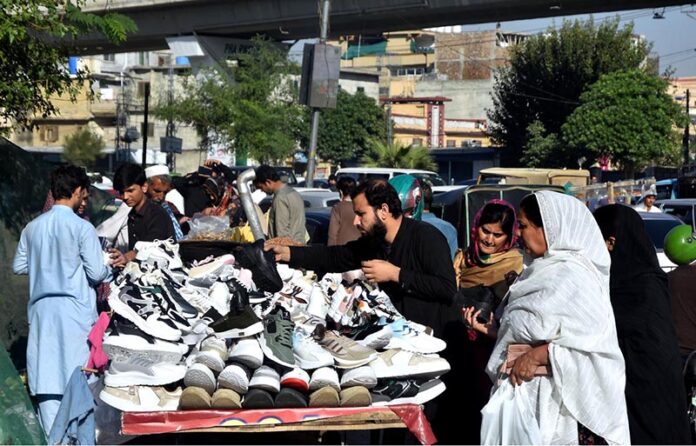 People selecting and purchasing used shoes from roadside vendor