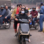 A woman rides an electric motorcycle towards her destination at Railway Station Chowk, wearing a mask to protect herself from the smog