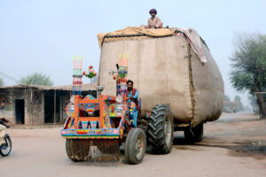 An overloaded tractor trolley carrying chaff (husk of wheat) on Kabirwala road while a person sits on the top