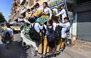 A view of overload school van as a large number of students traveling on the rooftop of a Suzuki van in a risky manner, posing a potential safety hazard, along Hirabad Road.
