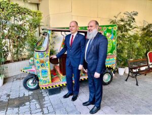 Federal Minister for Commerce Jam Kamal Khan and Belarusian Energy Minister Alexey Kushnarenko stand beside a handcrafted Pakistani rickshaw at the Pakistan-Belarus Business Forum 2024, discussing its intricate design and cultural significance.