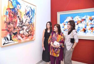 Women standing in front of the vibrant paintings of Mashkoor Raza at Farame The Art Gallery. As a renowned artist, Raza is known for blending modernist abstraction, particularly drawing from the traditional geometric patterns and spiritual symbols of his heritage.