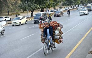 A vendor on his way, riding a bicycle loaded with handmade items, navigating through the Expressway in the Federal Capital.
