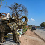 A vendor displays a majestic elephant statue along with other decorative items to attract customers at the roadside