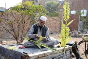 A worker is making decorative items with palm leaves to attract the customers at his setup.