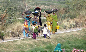 Village women carry freshly washed clothes home, highlighting rural life near the city bypass