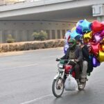 A vendor on the way on motorcycle carrying different shapes air-filled balloons in the Federal Capital