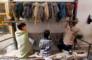 Children skillfully knitting carpets at their workplace at Afghan Colony.