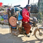 A motorcyclist vendor loaded with household items roams in the street to attract the customers in Latifabad