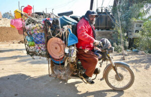 A motorcyclist vendor loaded with household items roams in the street to attract the customers in Latifabad