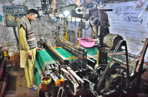 A worker is busy operating a power loom to prepare cloth in a local factory.