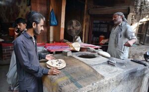Customer busy in collecting fresh bread as a naanbai bakes bread in a clay oven (tandoor) at Bacha Khan Chowk.