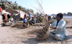 Artisan making baskets from dry tree branches at a roadside setup.