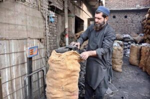 A vendor weighs and packs coal into sacks for sale at his setup.