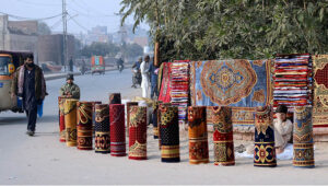 A vendor is displaying the carpets to attract customers at his roadside setup.