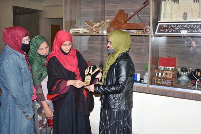 A craftswoman showcases her intricately handmade jewelry to a visitor at her stall during a Craft Exhibition organized by the Faisalabad Arts Council