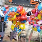 A vendor selling colorful helium-filled inflatable balloons and toys at a roadside stall