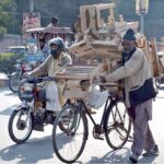A vendor moving his bicycle loaded with wooden stools on the way going to local market