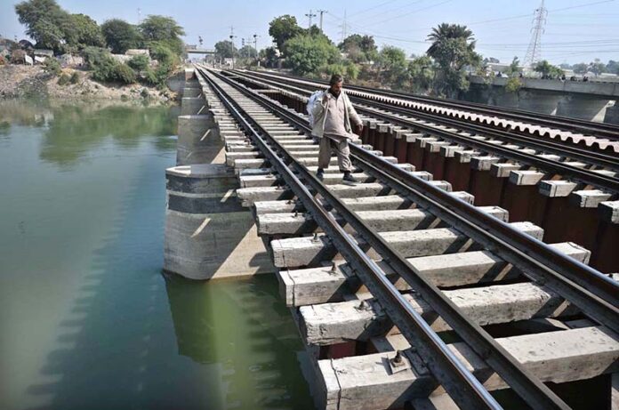A man crossing Phuleli Canal on a railway bridge, risking a potential mishap at Tando Yousuf