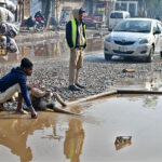 Workers use a motor pump to clear accumulated rainwater from the road, ensuring smoother passage for both traffic and pedestrians