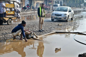 Workers use a motor pump to clear accumulated rainwater from the road, ensuring smoother passage for both traffic and pedestrians